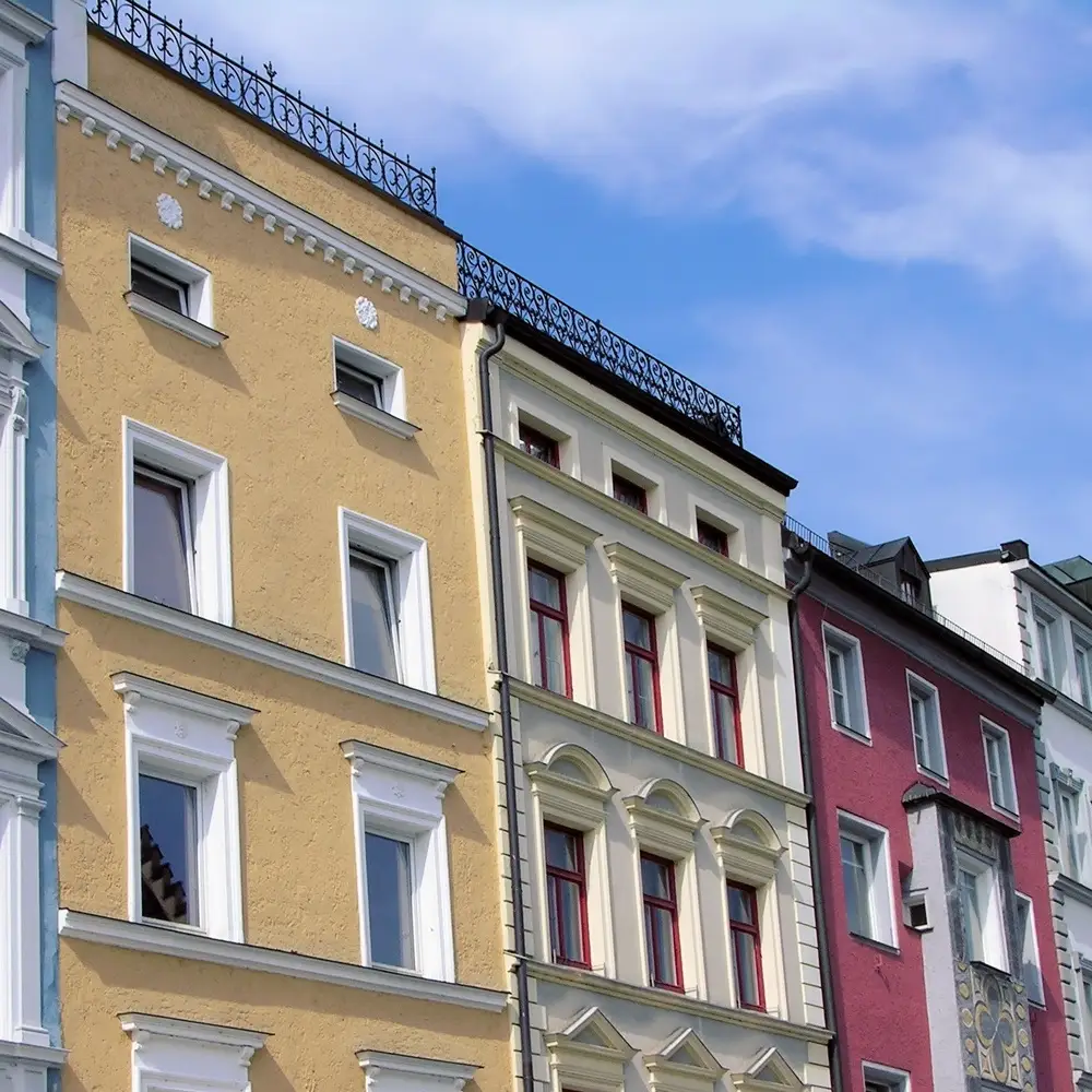 Raimund Klein Immobilien 3 Farbige Altbauten mit Stuckfassade und schmiedeeisernen Balkongeländern in einer städtischen Häuserzeile.