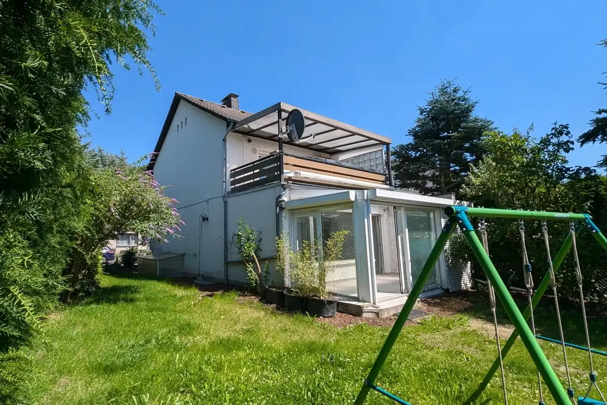 Rückseite eines Einfamilienhauses mit Wintergarten und Balkon.